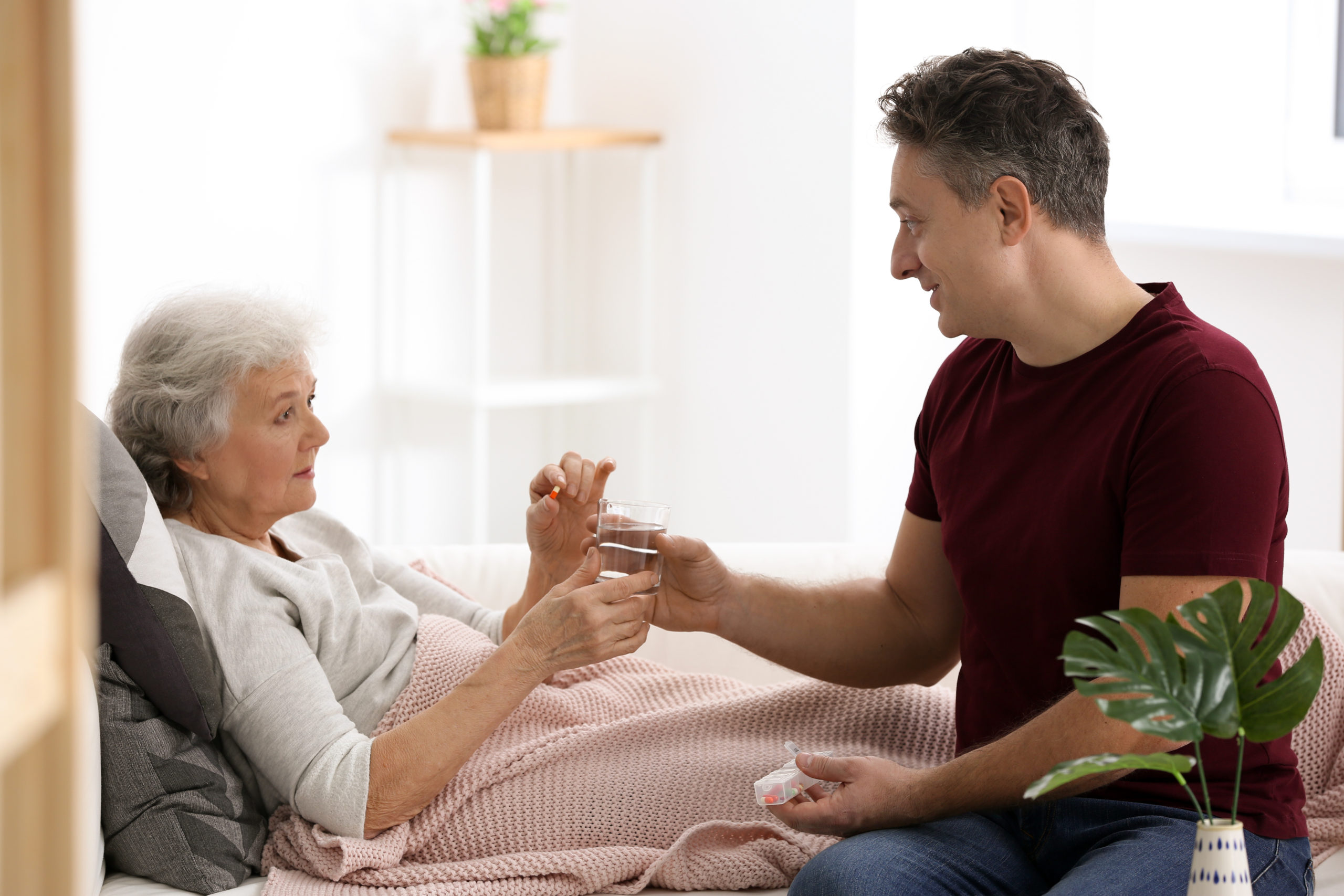 Man giving pill to elderly woman, indoors